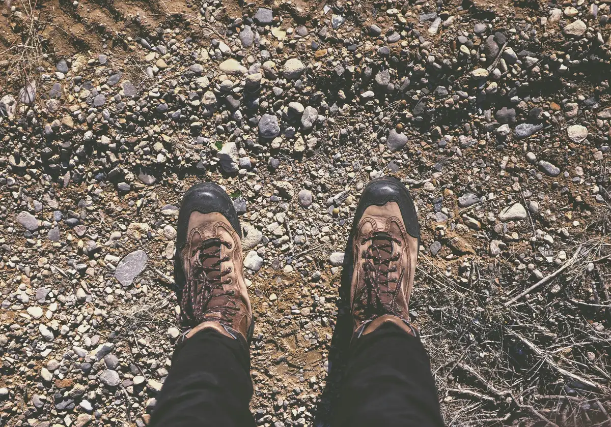 person wearing brown shoes standing on dirt and stone ground