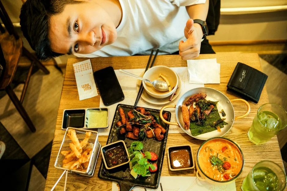 Young man smiling with a variety of Asian dishes at a restaurant, showcasing a delicious dining experience.