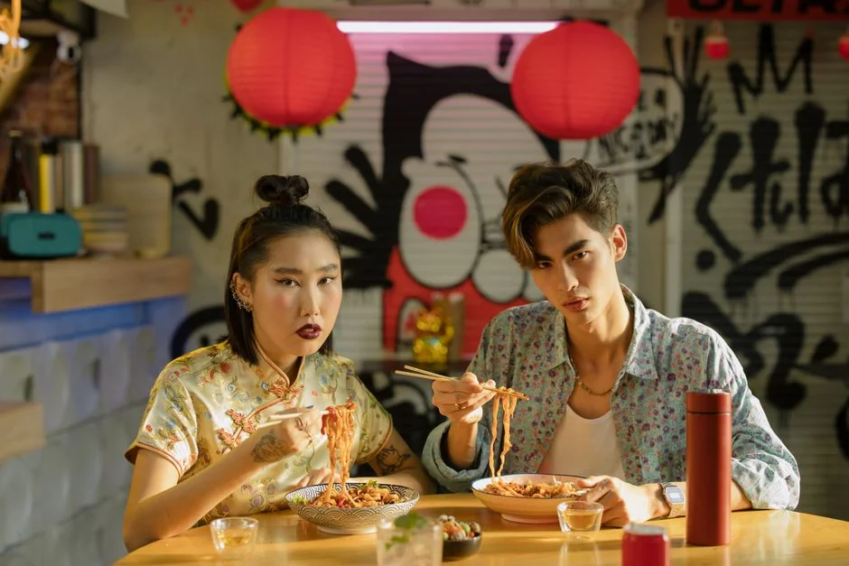 Young couple savoring noodles together indoors, capturing a modern Asian dining experience.