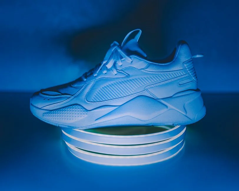 A stylish white sneaker in blue lighting, showcased on an illuminated stand, highlighting modern fashion trends.