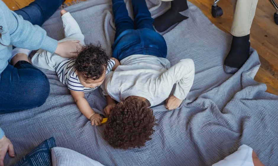 From above of small baby and kid lying on blanket on parquet and crop parents looking after them