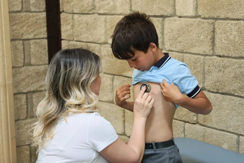 A female doctor uses a stethoscope to listen to a young boy's heartbeat, conducting a health check outdoors.