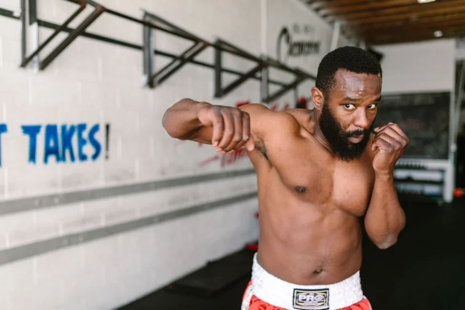 Muscular African American man practicing boxing in a gym setting, showing focus and determination.
