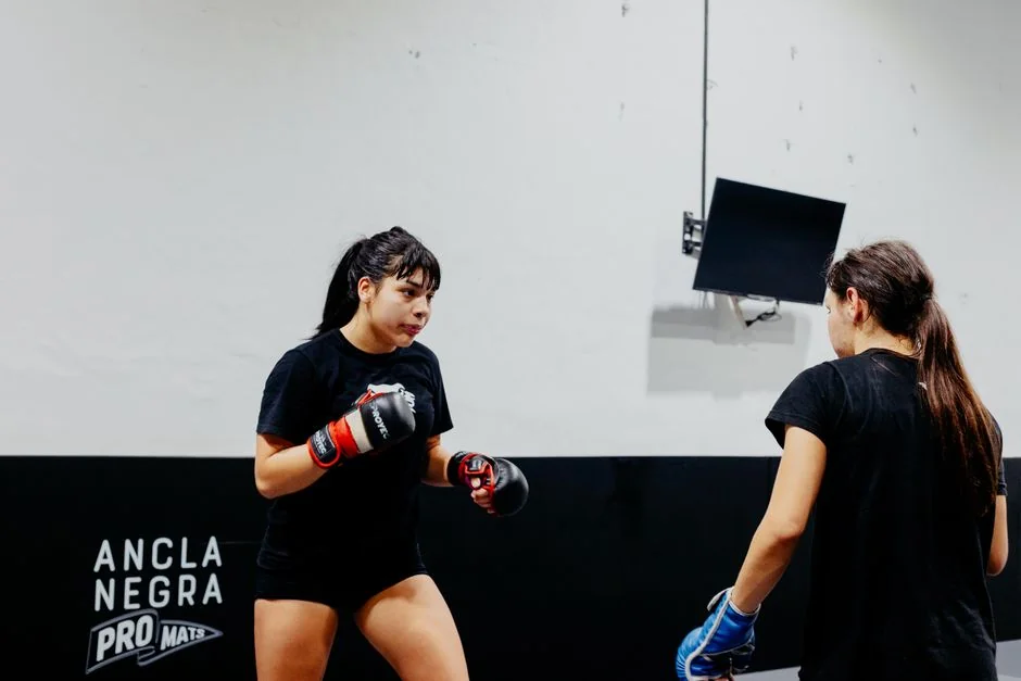 Two women engaged in martial arts training indoors, showcasing strength and focus.