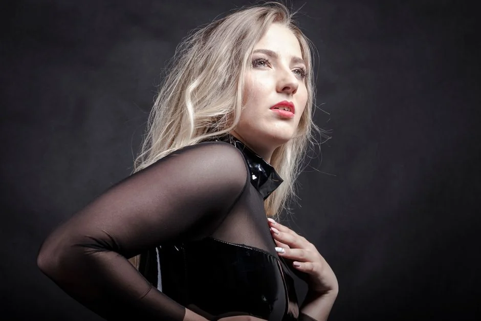 Stylish portrait of a woman wearing a black sheer and latex outfit against a dark background.